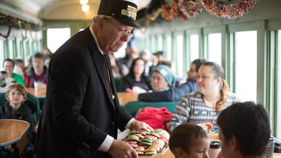 A conductor offers a platter of cookies to a family on the train