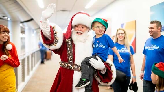 Wish kid Brantley smiling while Santa is waving and holding him.