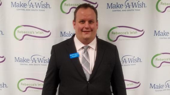 Matt standing in front of Make-A-Wish sign at event.