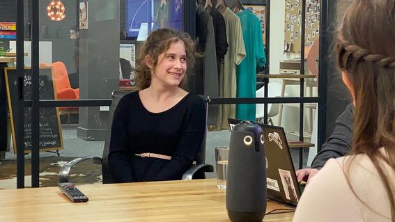 Young woman smiles at someone off-camera, while seated at table.