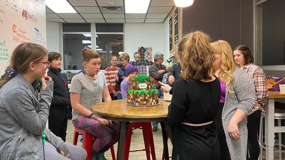 People gather around a minecraft-themed cake on a table