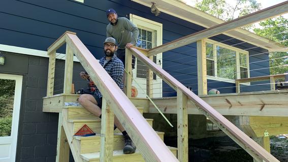 Two men pause to smile while working to build stairs to a deck