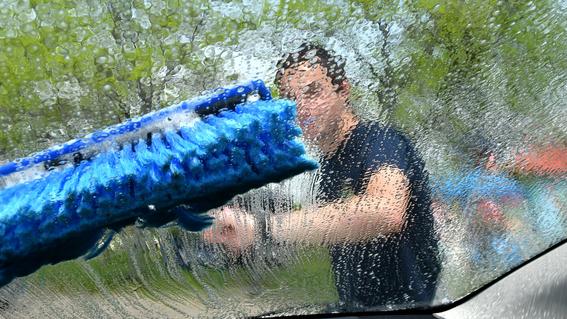 a large brush head is seen from inside a car, as a man washes the windshield