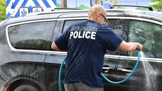 a man in a blue shirt reading "police" sprays down a soapy SUV