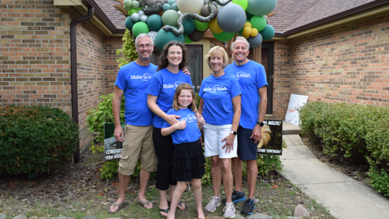 parents and volunteers with Mazie smiling in front of balloon sculpture
