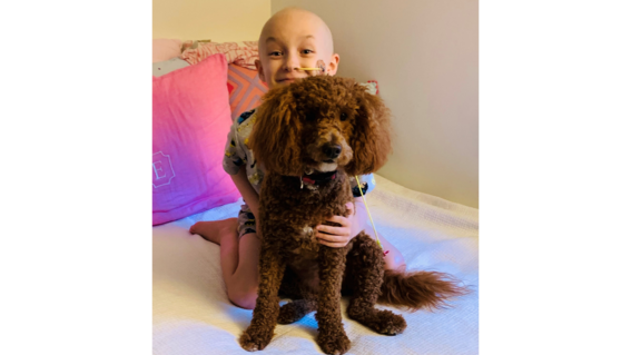 Eleanor and her goldendoodle, Willow, smiling at the camera on Eleanor's bed