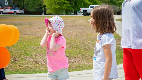 Izzy wearing a pink shirt and pink/white bucket hat holding her head in surprise