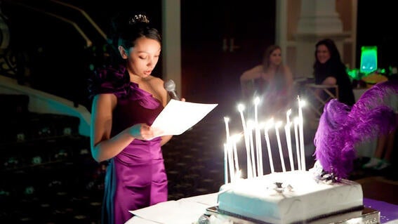 Nicole wearing a purple dress making a speech in front of her cake and candles