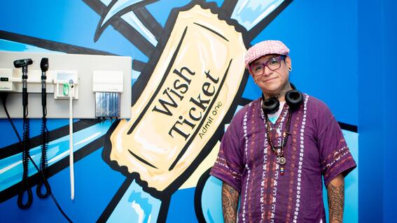Juan Muniz stands beside his original mural in the Make-A-Wish-themed exam room.