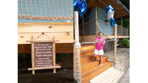 A sign declaring how special Libby's treehouse is, and a photo of Libby smiling big as she's cutting the ribbon to her treehouse