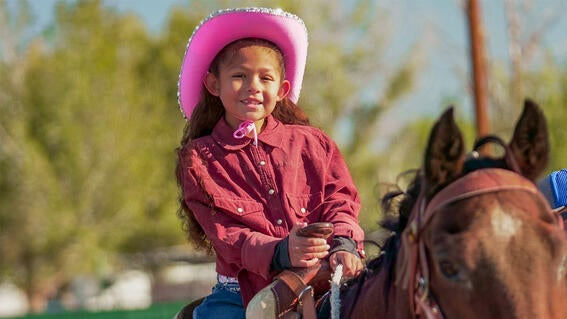 Wish kid Annie dressed as a cowgirl, complete with pink hat, smiles from atop a horse