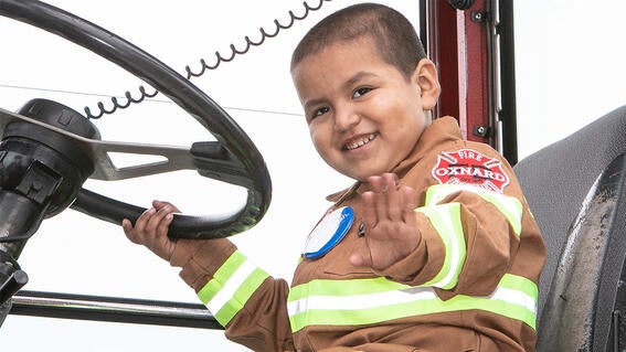 Sergio dressed as firefighter smiles and waves from the firetruck