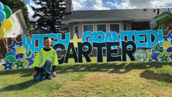 At the end of his wish day and after having picked up the trash from his own home, Carter smiles in front of a sign in his front yard that reads "WISH GRANTED!"