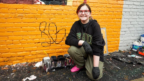 Josie posing next to her signature on the mural