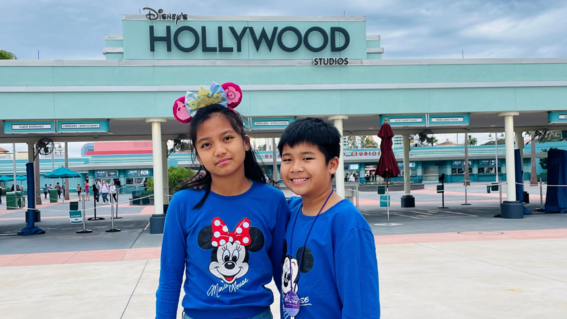Jeshua and his sister stand in front of hollywood studios sign in blue shirts.