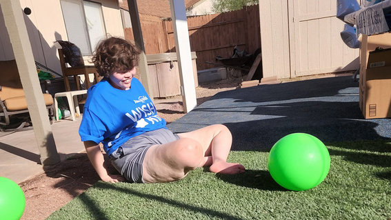 Lily sits on the ground and enjoys the features of her sensory backyard.