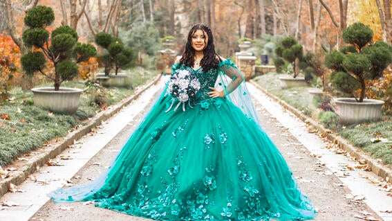 Wish kid Emely standing outside in a beautiful green ballgown holding a bouquet of flowers for her quinceanera