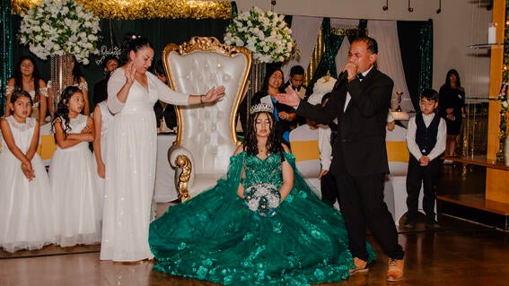 Emely seated as her parents share a blessing standing on either side of her