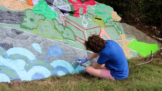 Nate works on the mural in Northbridge, spray painting bright colors onto an original drawing by Ben Jundanian
