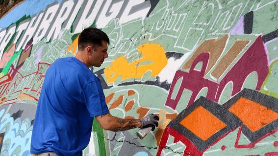 Ben works on the mural in Northbridge, spray painting bright colors onto an original drawing by Ben Jundanian