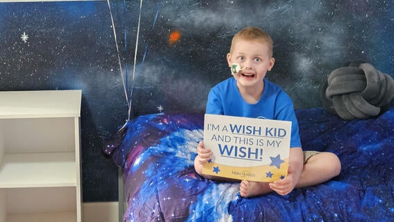 Aleksander sits in his galaxy-themed sensory room and holds his wish sign.
