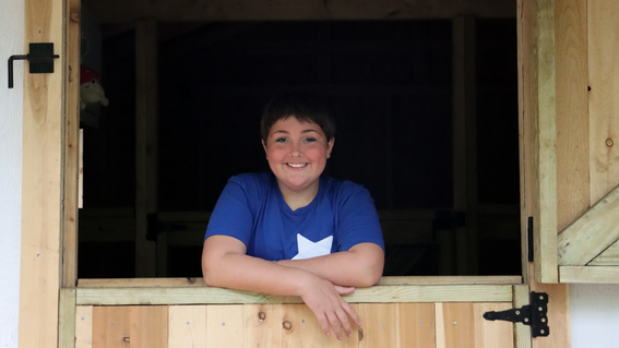 Wish kid Maddie posing in the doorway of her barn, looking at the camera