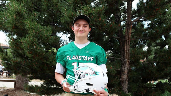 Stephen stands in front of a pine tree in his football uniform.