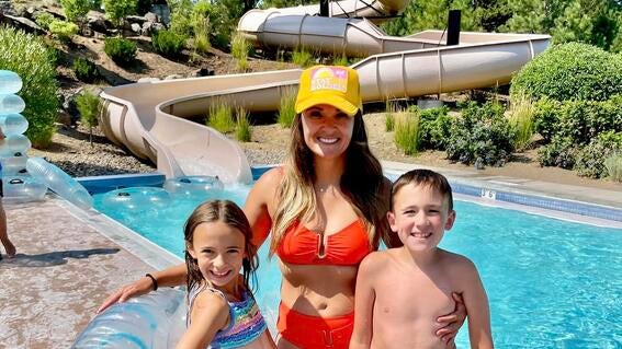 woman and two children looking at camera smiling in swim attire in front of a water park slide.