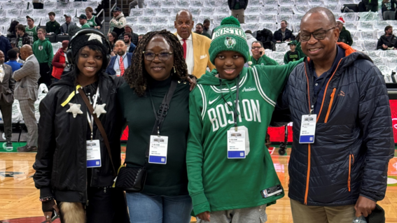 Ikenna & his family pose at center court for a photo, with Celtics Legend Cedric Maxwell on his way to photobomb