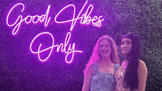 Bria and cousin standing in front of neon sign that reads "Good Vibes Only"