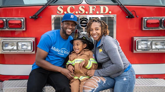 Jayce and his parents sitting in front of the firetruck