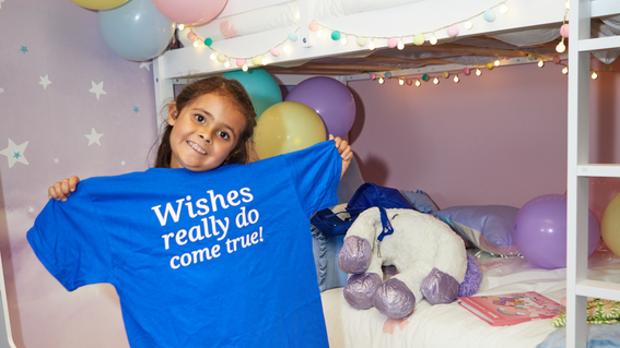 Emma holding up a Make-A-Wish tee shirt that reads "wishes really do come true"