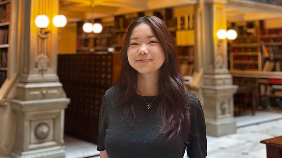 Ziyan stands in a library with books and marble pillars in the background.