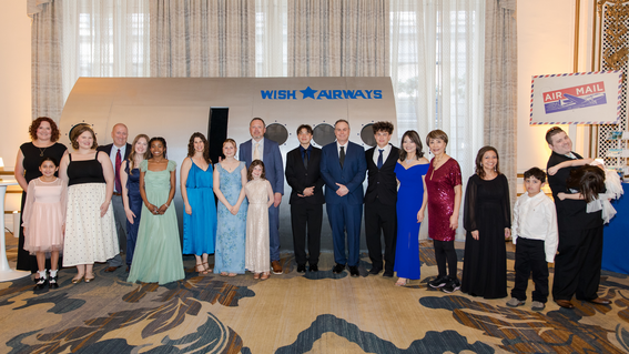 Featured wish kids Suriha, Devan, Corbin, and Elana and their families pose in front of the Wish Airways wall at the Sky Lounge Welcome Reception.