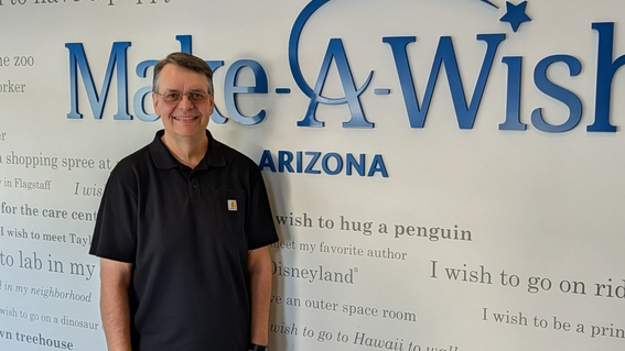 Eric Lardy, March Volunteer of the Month, in front of Wish Wall