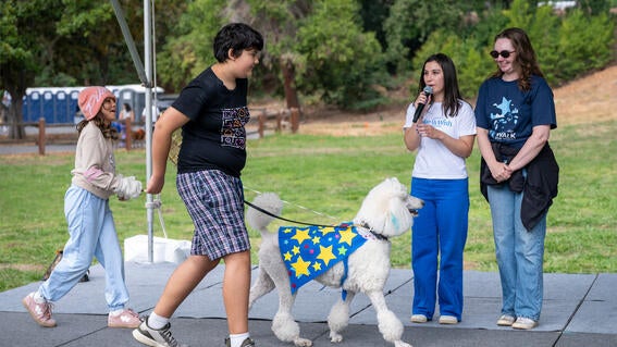 A poodle in costume and two kids cross the stage