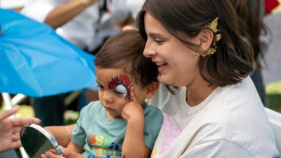 A child and parent admire Spider-Man face paint in a handheld mirror