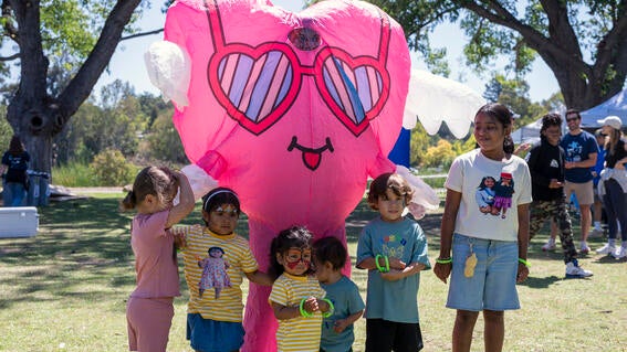 Children stand with a pink heart mascot character