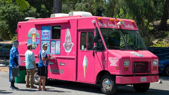 Walkers stand in line in front of a pink food truck selling ice cream