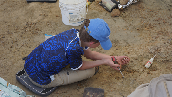 Ian sitting on the ground digging for dinosaur fossils