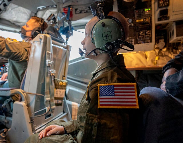 Wish kid Korbyn, wearing a flight suit, sits in the middle of the cockpit for a KC-135 Stratotanker plane.