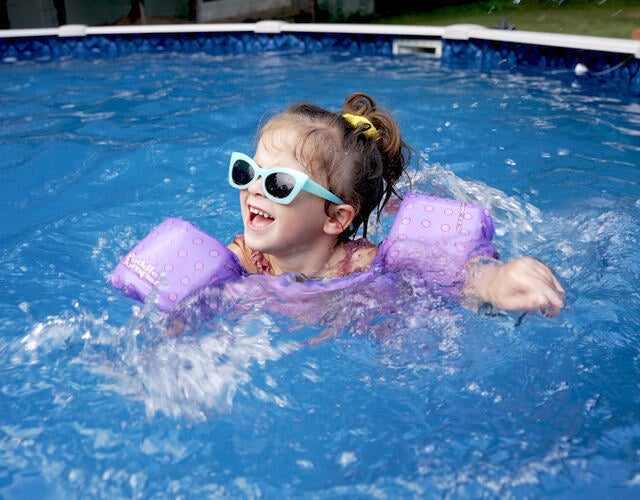 wish kid Alice swimming in above-ground pool wearing purple floaties and blue sunglasses