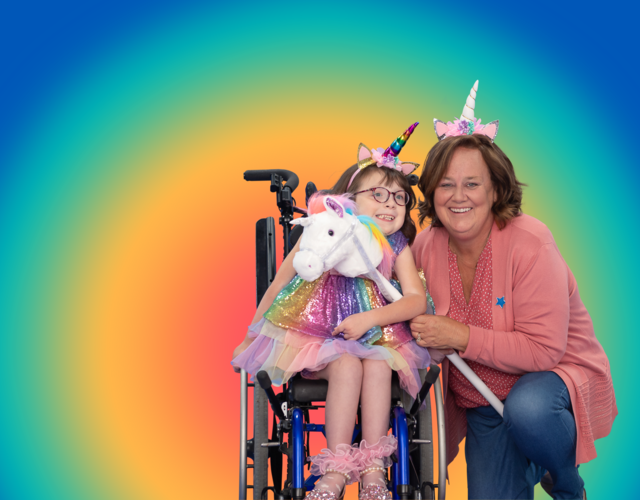 Wish kid Mya and WishMaker Cheryl wearing unicorn horns in front of a rainbow background