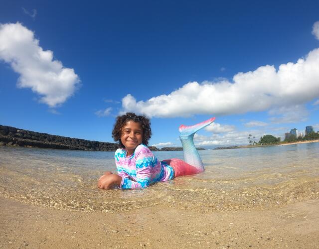 Wish kid Chrischell in a mermaid tail laying in the water on the beach