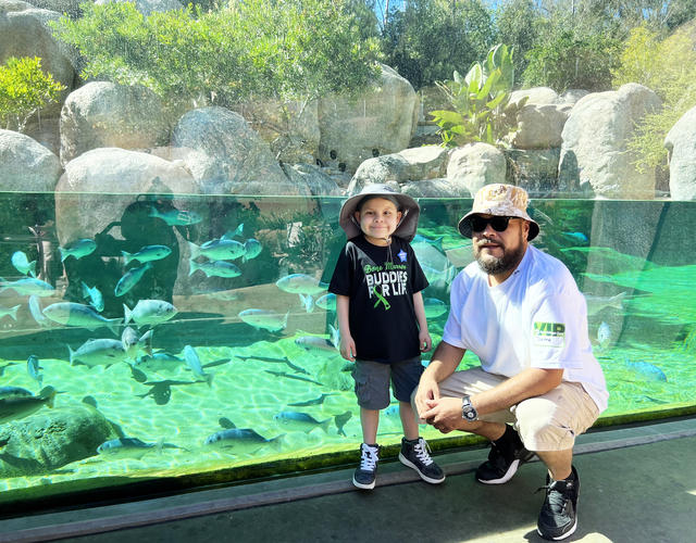 Jaime and his dad in front of an aquarium with fish at the San Diego Zoo