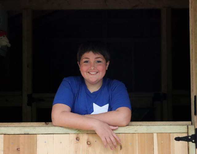 Wish kid Maddie posing in the doorway of her barn, looking at the camera
