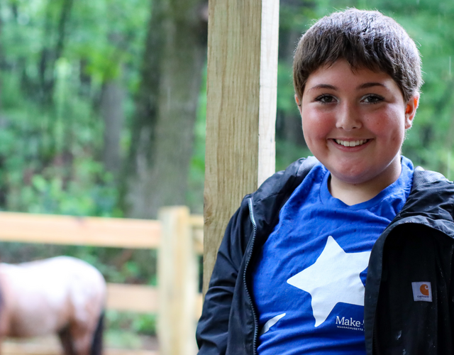Wish kid Maddie smiling at the camera with one of her mini horses in the background