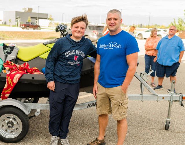 A wish child and volunteer in front of a jet ski
