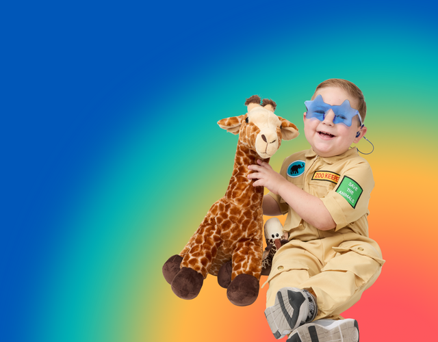 A child in a zoo keeper costume holds a plush giraffe, wearing blue star-shaped glasses and hearing aids against a vibrant rainbow gradient background.