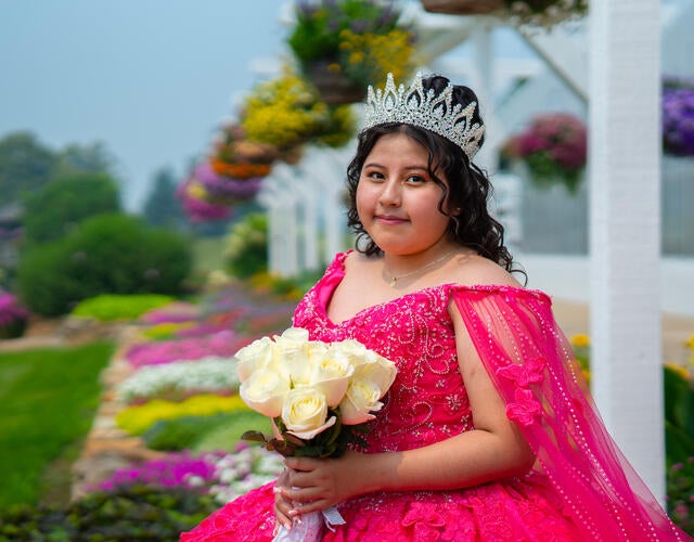 Alison holding a bundle of flowers standing in a beautiful garden in her pink dress and crown.